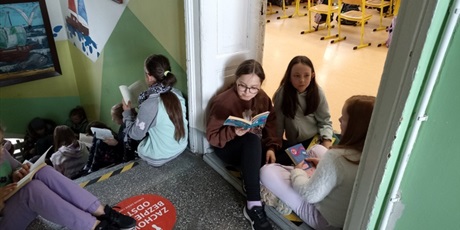 Powiększ grafikę: Grupa uczniów czyta na schodach.