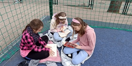 Powiększ grafikę: Trzy uczennice czytają na boisku.