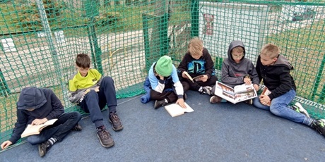 Powiększ grafikę: Grupa chłopców czyta na boisku.