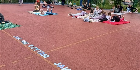 Powiększ grafikę: Uczniowie czytają na boisku.