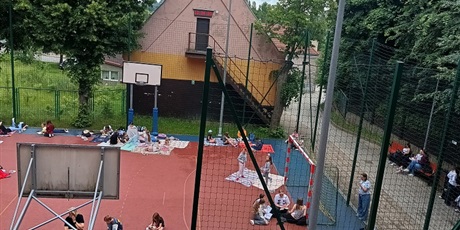 Powiększ grafikę: Boisko z czytającymi uczniami.