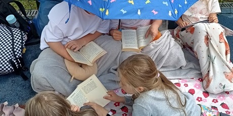 Powiększ grafikę: Uczniowie czytają pod parasolem.
